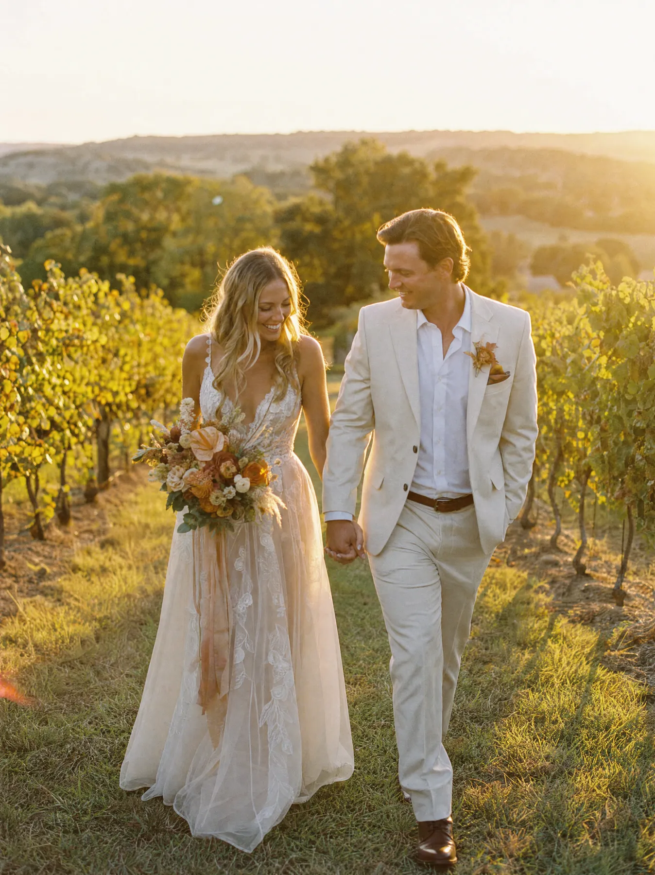 Couple walking hand in hand through a Hill Country vineyard at golden hour